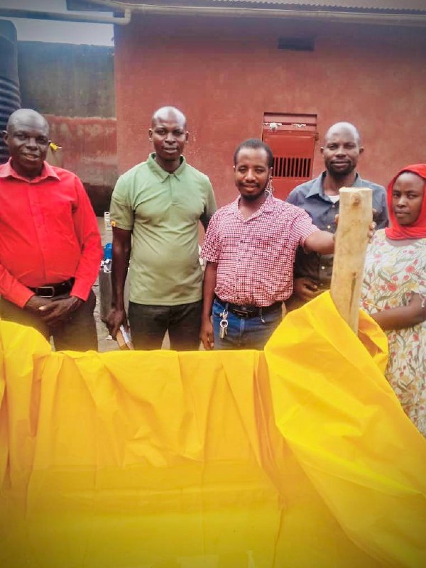 People standing behind the timber-supported, yellow tarpaulin-lined baptism pool at Kagadi Prison.
