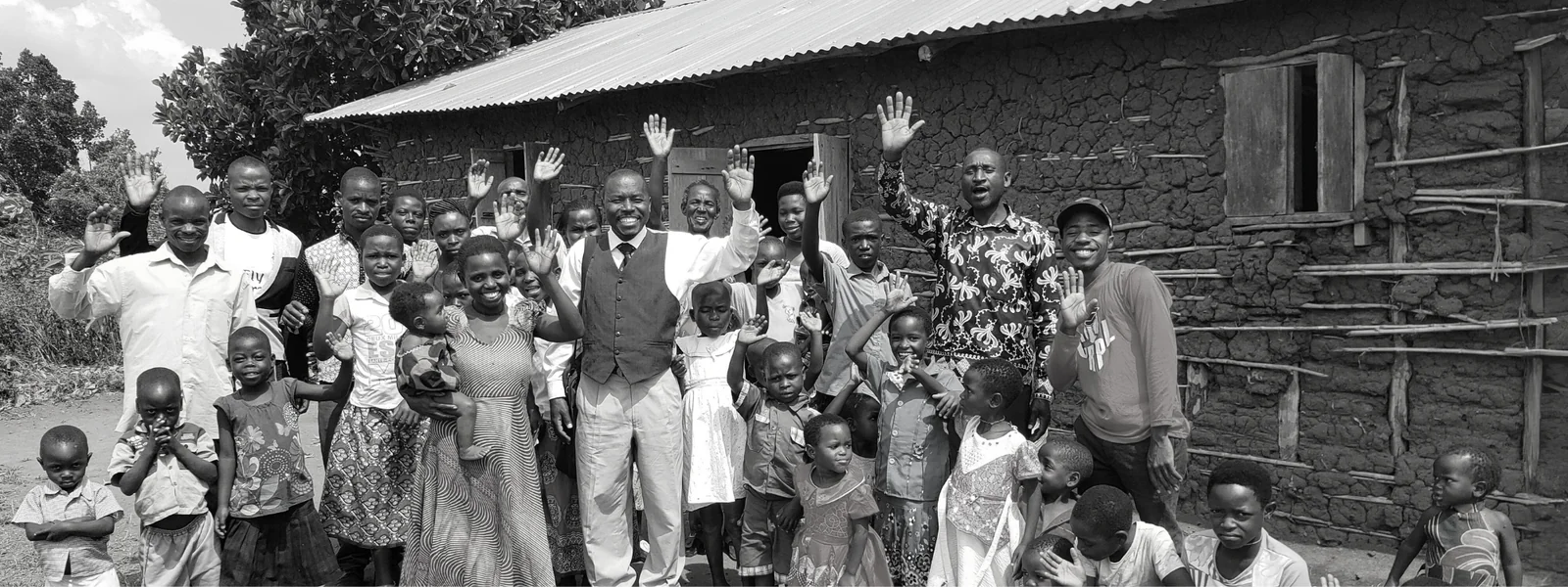 A church community of adults and children waving together outside a brick church building.