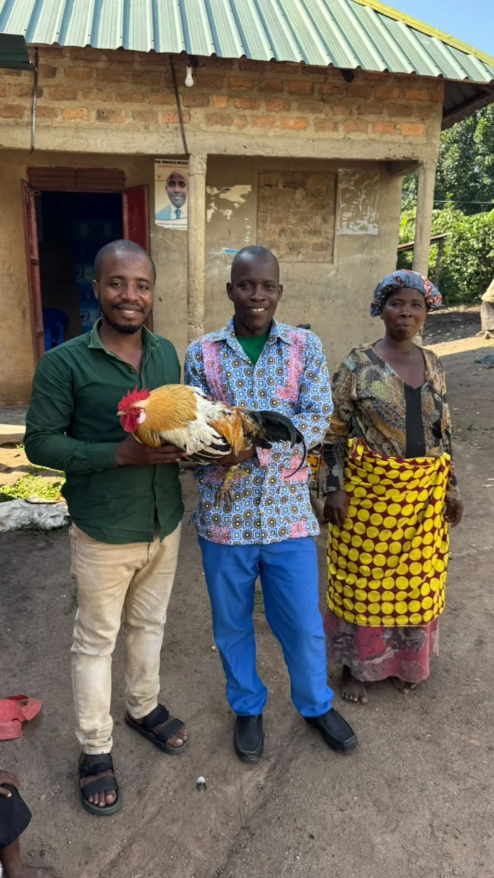 Naphtali holding a rooster beside Pastor Joseph and another adult during the visit.